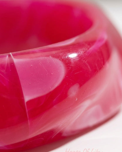 Thick, hot pink and white marbled acrylic statement bangle bracelet with a glossy finish.
