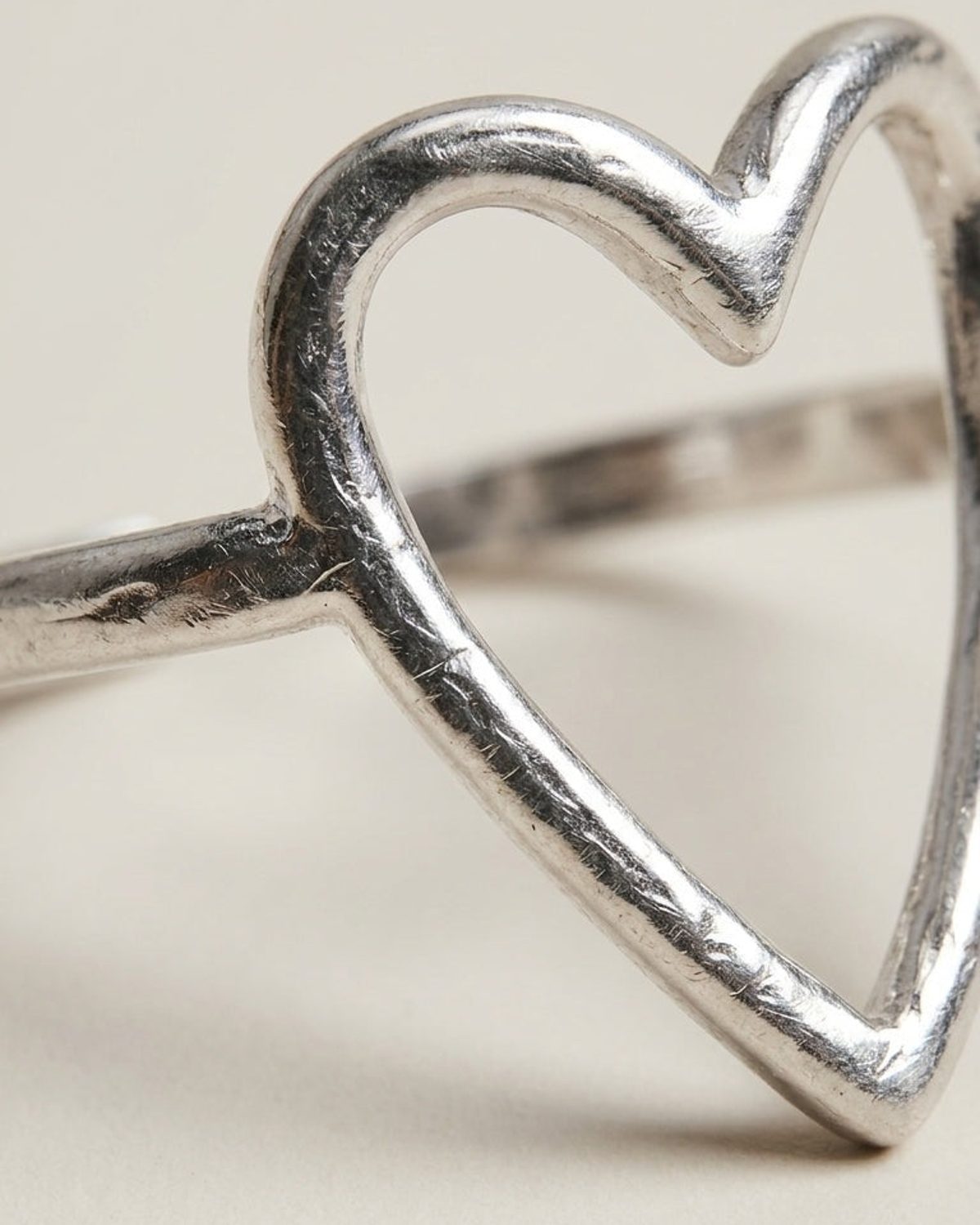 A close-up of a silver ring featuring a textured heart-shaped outline on a neutral background.