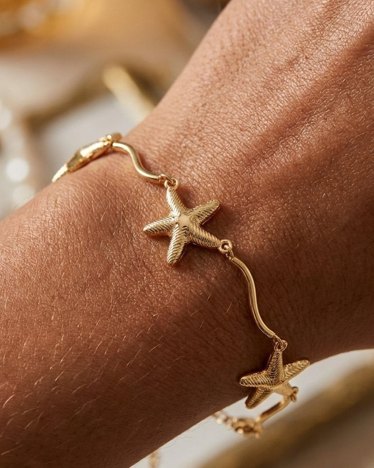 A gold metallic bracelet with textured starfish charms worn around a person's wrist.