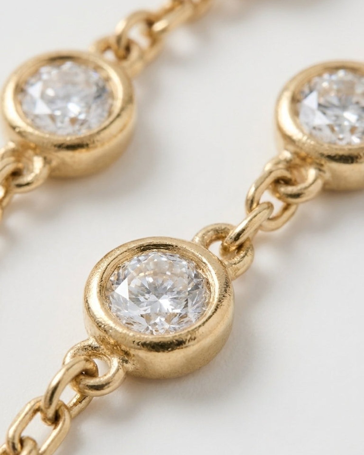 Close-up of a gold chain necklace featuring bezel-set round faceted clear stones.