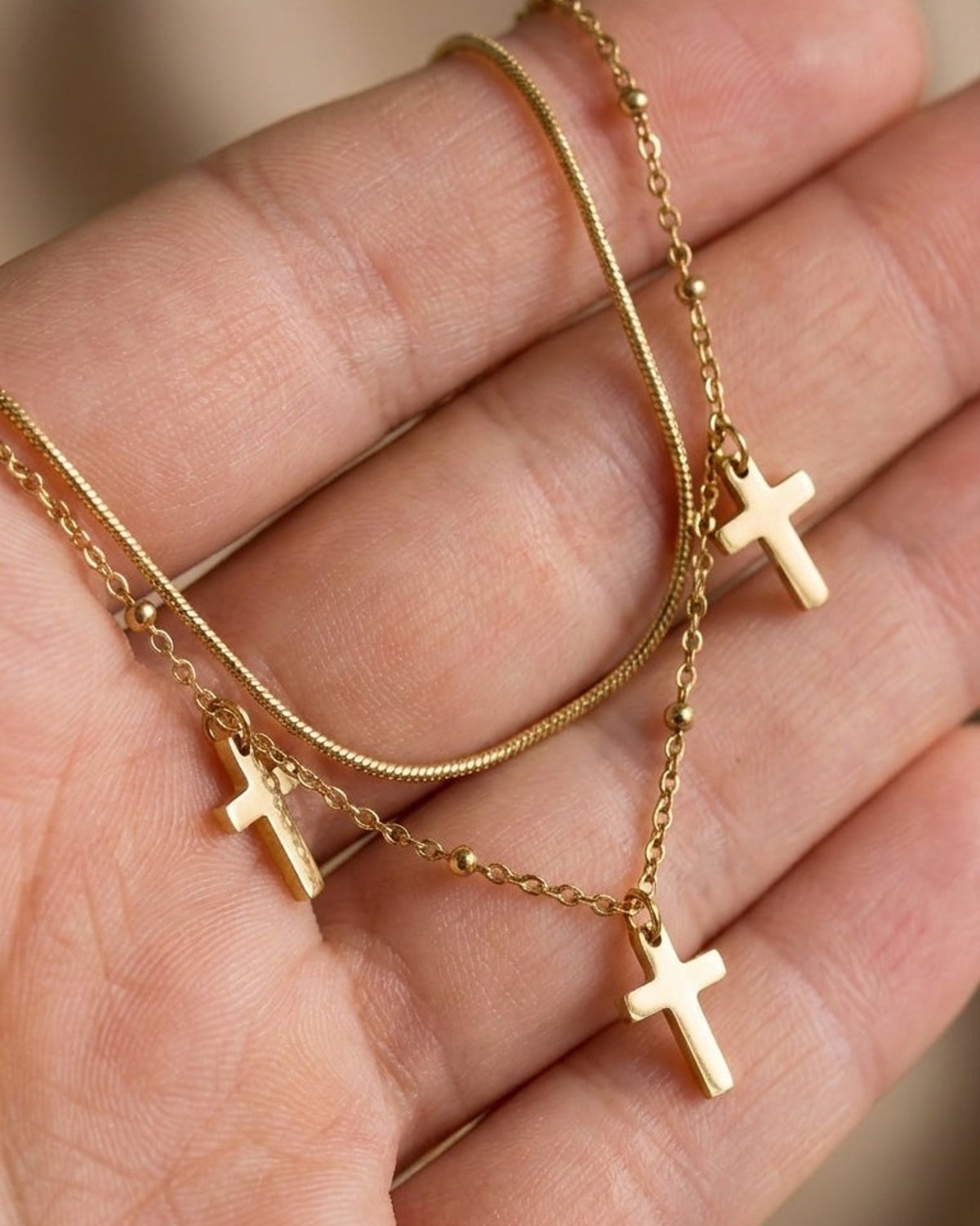 Gold layered chain necklace with three cross pendants held in a hand, showcasing a dark academia style.