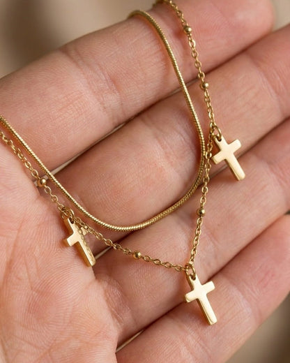 Gold layered chain necklace with three cross pendants held in a hand, showcasing a dark academia style.