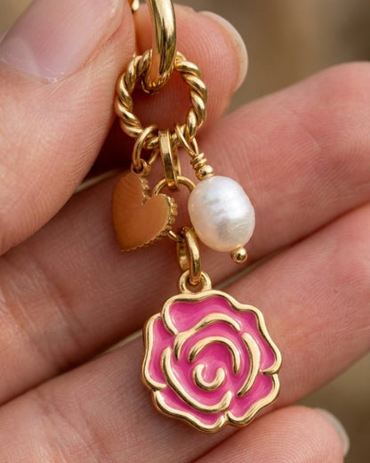 Gold drop earring with a pink rose charm, heart pendant, and pearl bead held in hand.