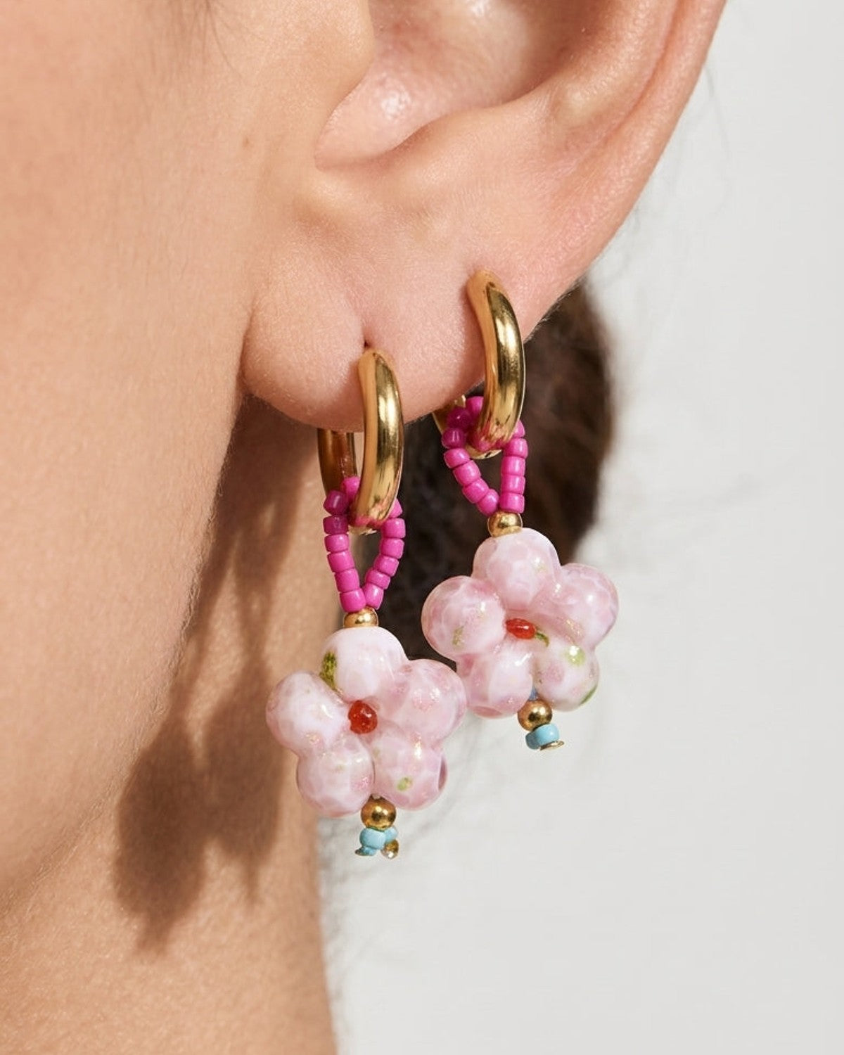 Gold hoop earrings with pink beaded loops holding pink marbled flower pendants worn on an earlobe.