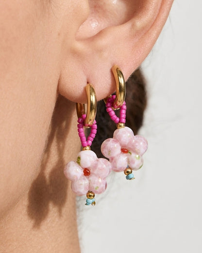 Gold hoop earrings with pink beaded loops holding pink marbled flower pendants worn on an earlobe.