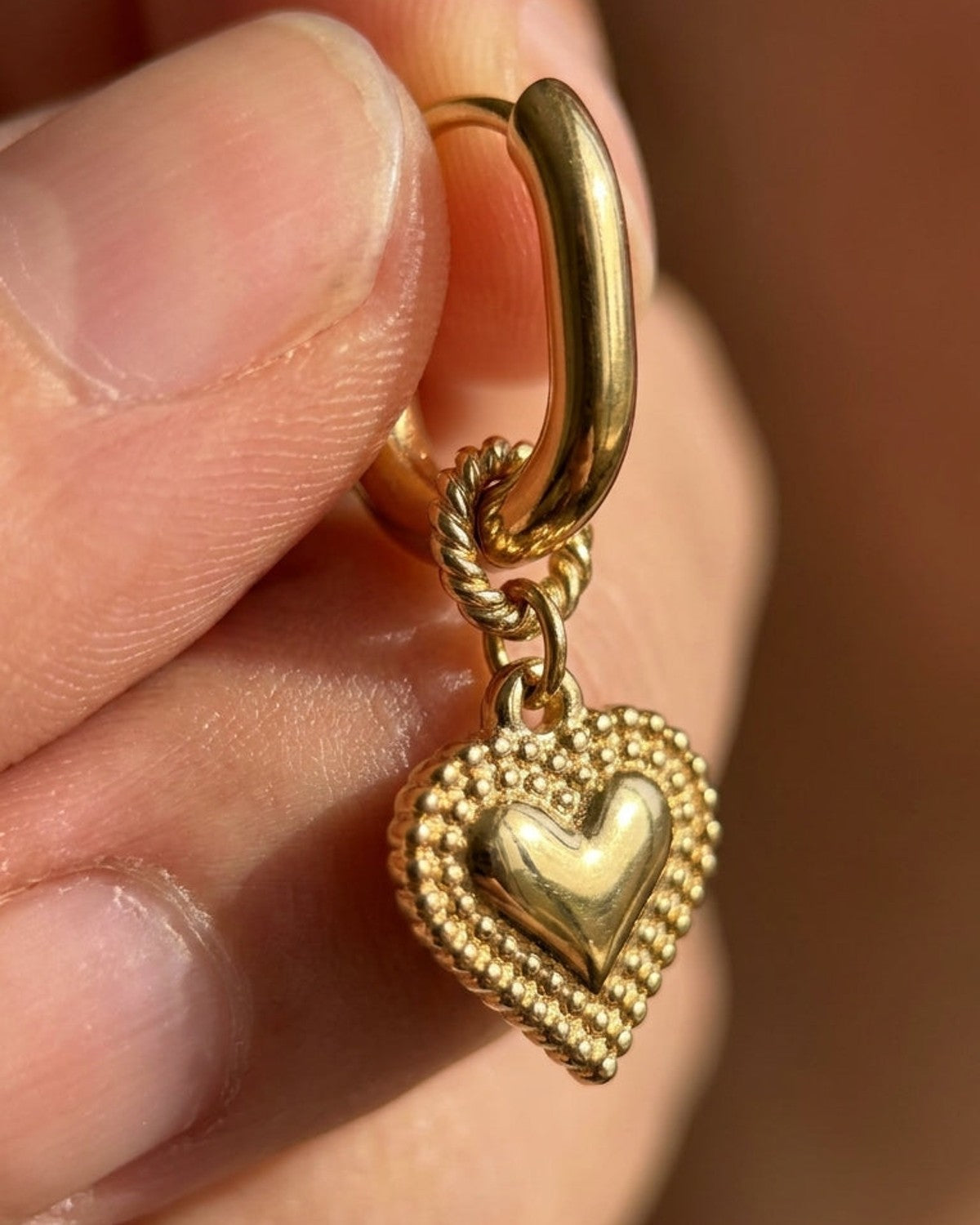 Gold hoop earring with a textured heart charm featuring a raised central heart and beaded border.