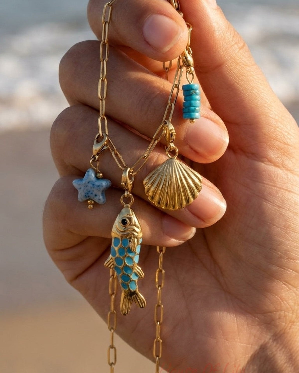 Gold paperclip chain charm bracelet with fish, seashell, starfish, and turquoise beads.