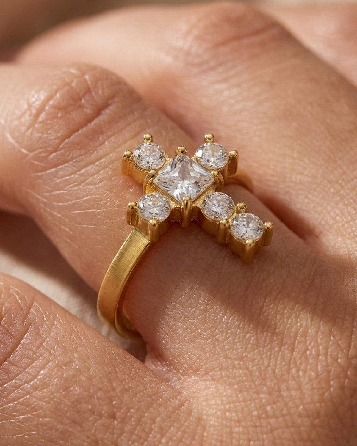 Gold ring with a cross-shaped setting of clear cubic zirconia stones on a finger.