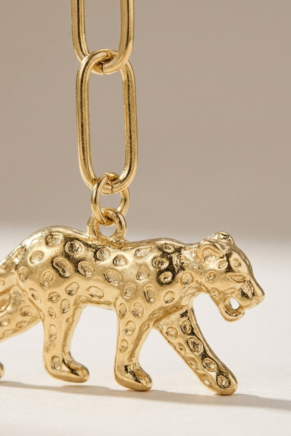 Gold pendant necklace featuring a textured leopard with engraved spots suspended from an elongated link chain.