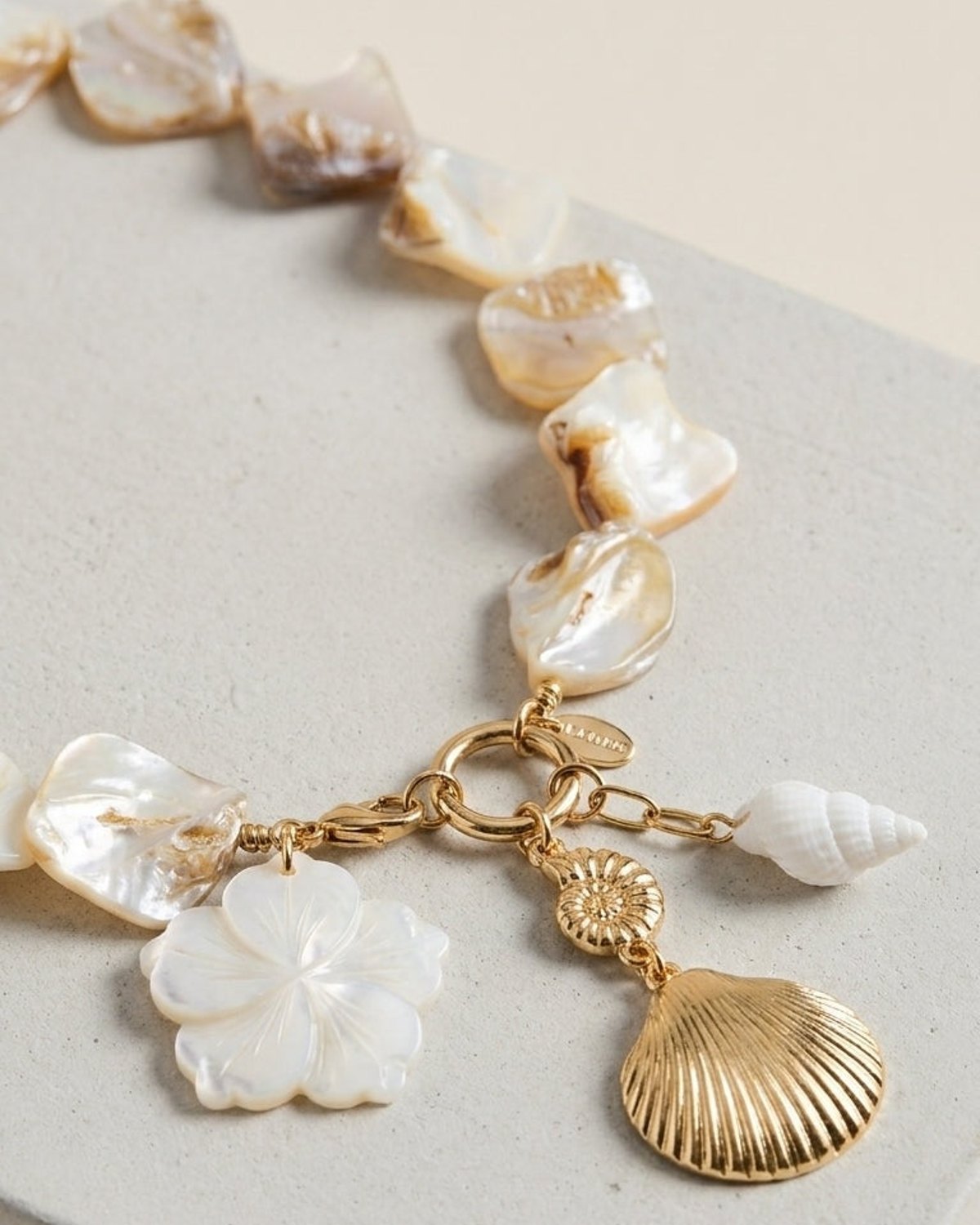 House Of Lily Seashell Charm Statement necklace with gold chain and mother-of-pearl charms on a grey surface.