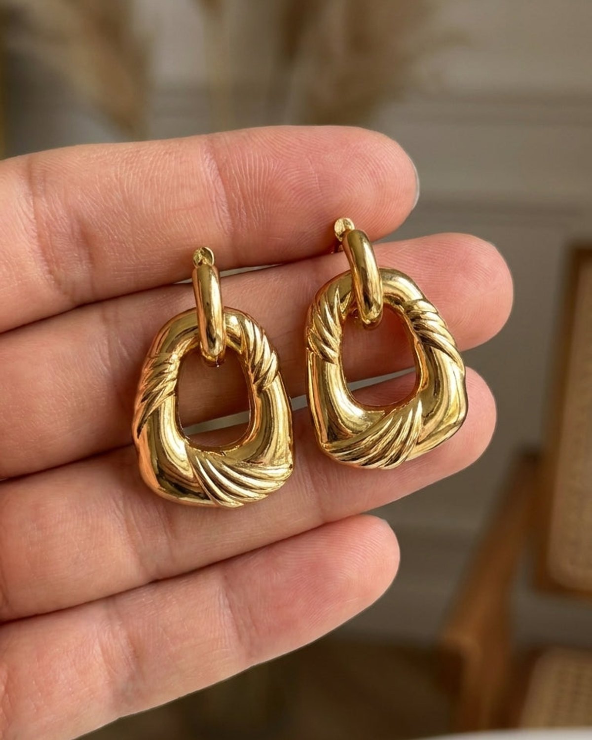 Gold irregular drop earrings with a textured, twisted hoop design held in a hand.