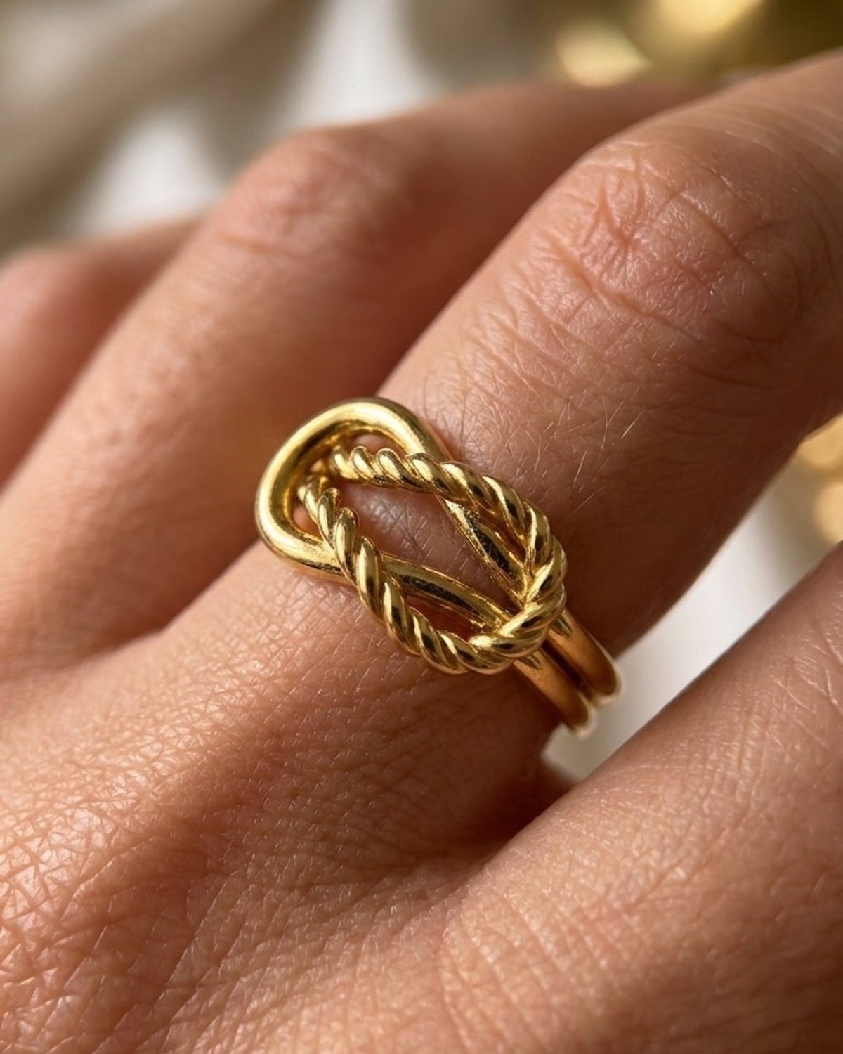 House Of Lily gold-tone statement ring shaped like a twisted rope knot, worn on a finger.