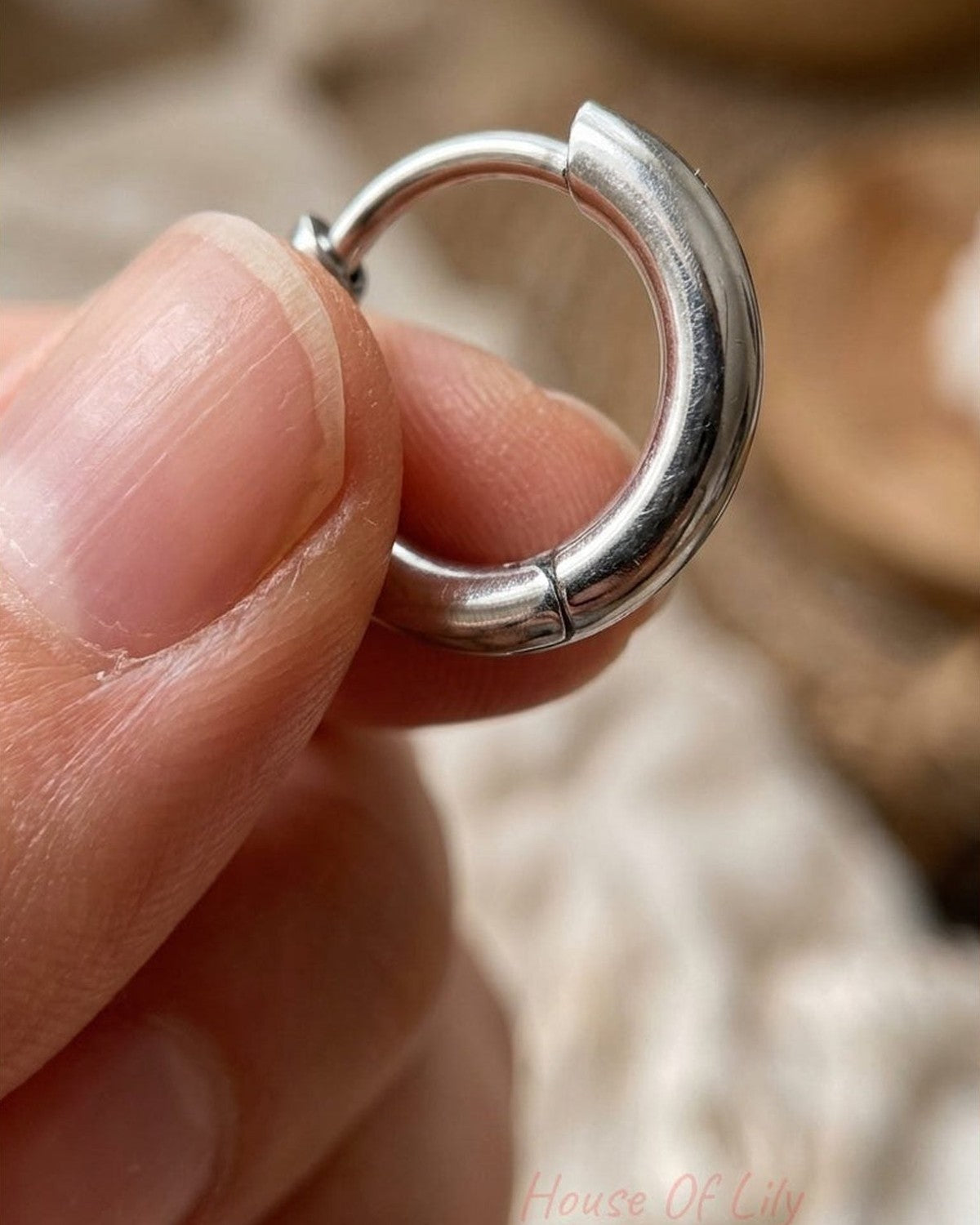 Small, polished silver hoop earring with a hinge clasp, held between thumb and forefinger.