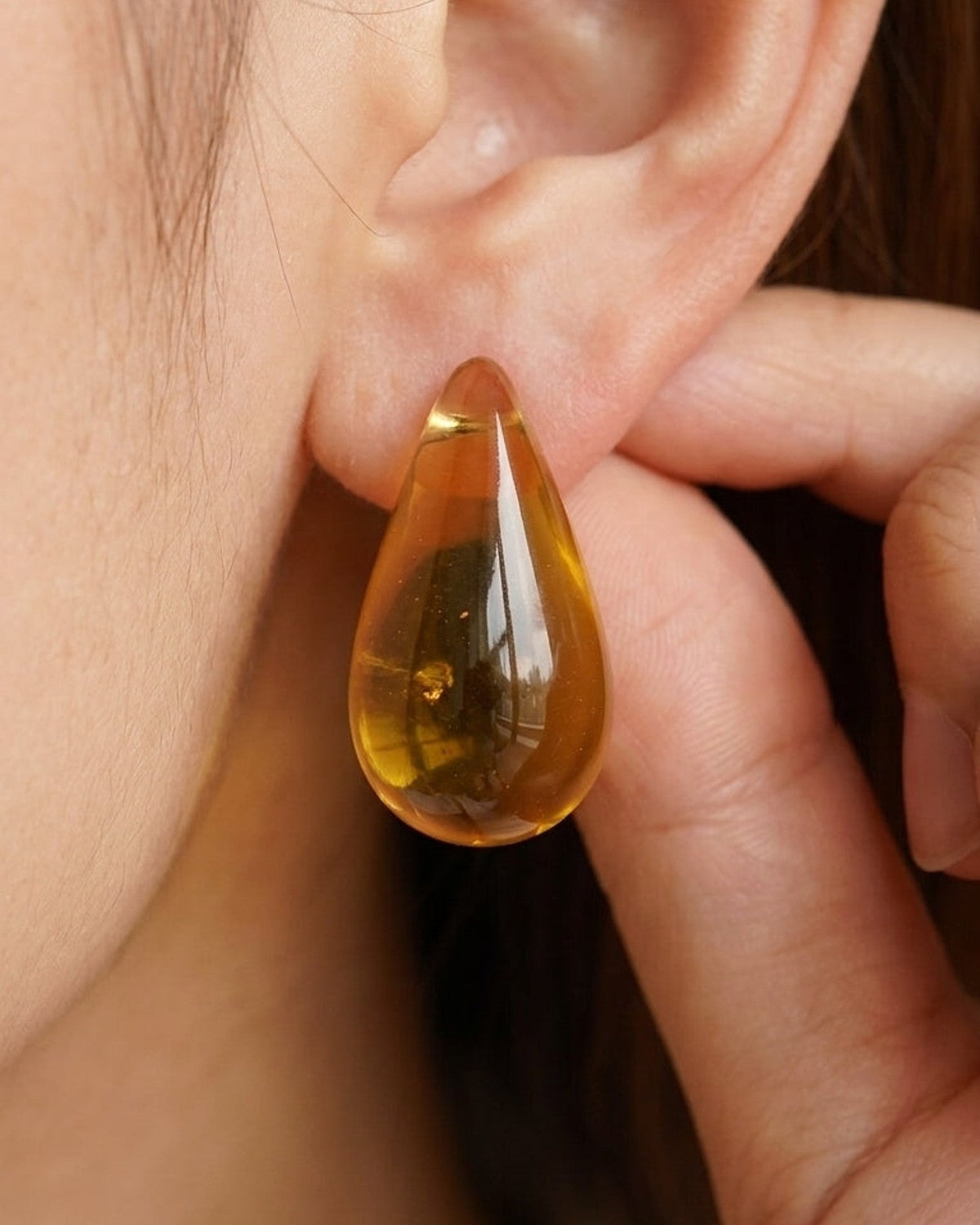 Amber resin droplet stud earrings worn on an earlobe, featuring a glossy teardrop shape.