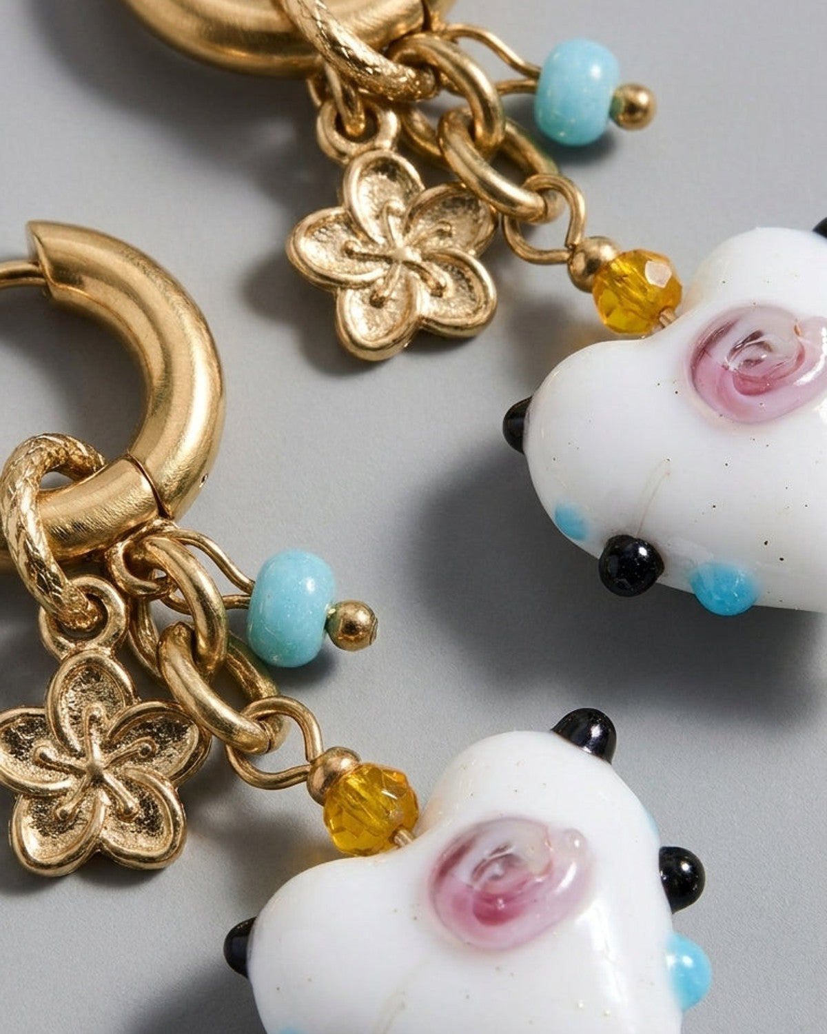 Gold-tone hoop drop earrings with white glass heart charms, blue beads, yellow beads, and gold-tone flower charms.