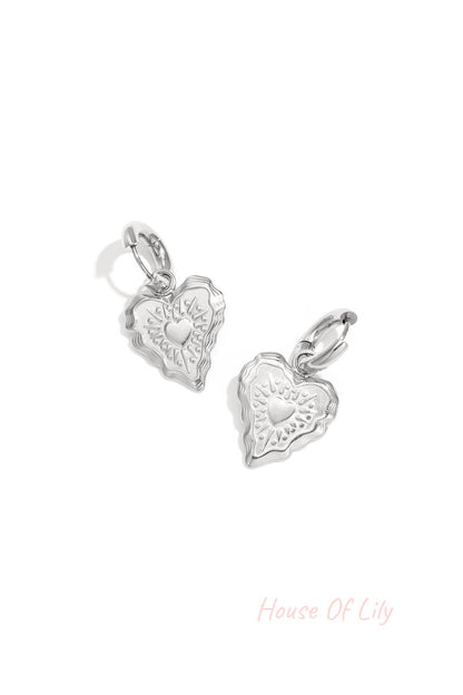 Close-up of silver heart charm hoop earrings with embossed detailing on a white background