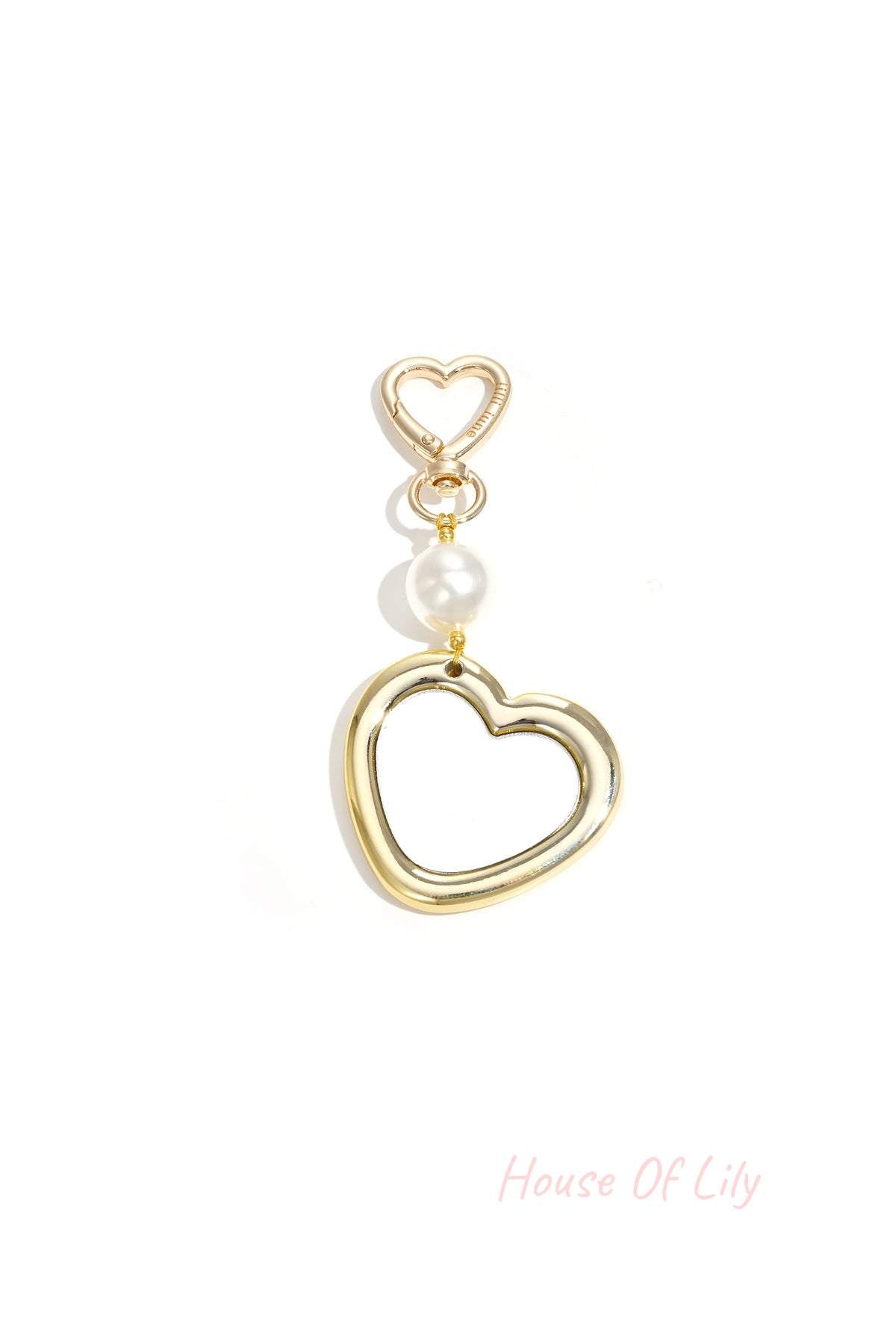 Gold heart-shaped bag charm with a reflective mirror finish, accented by a single white pearl on a heart-shaped clasp.