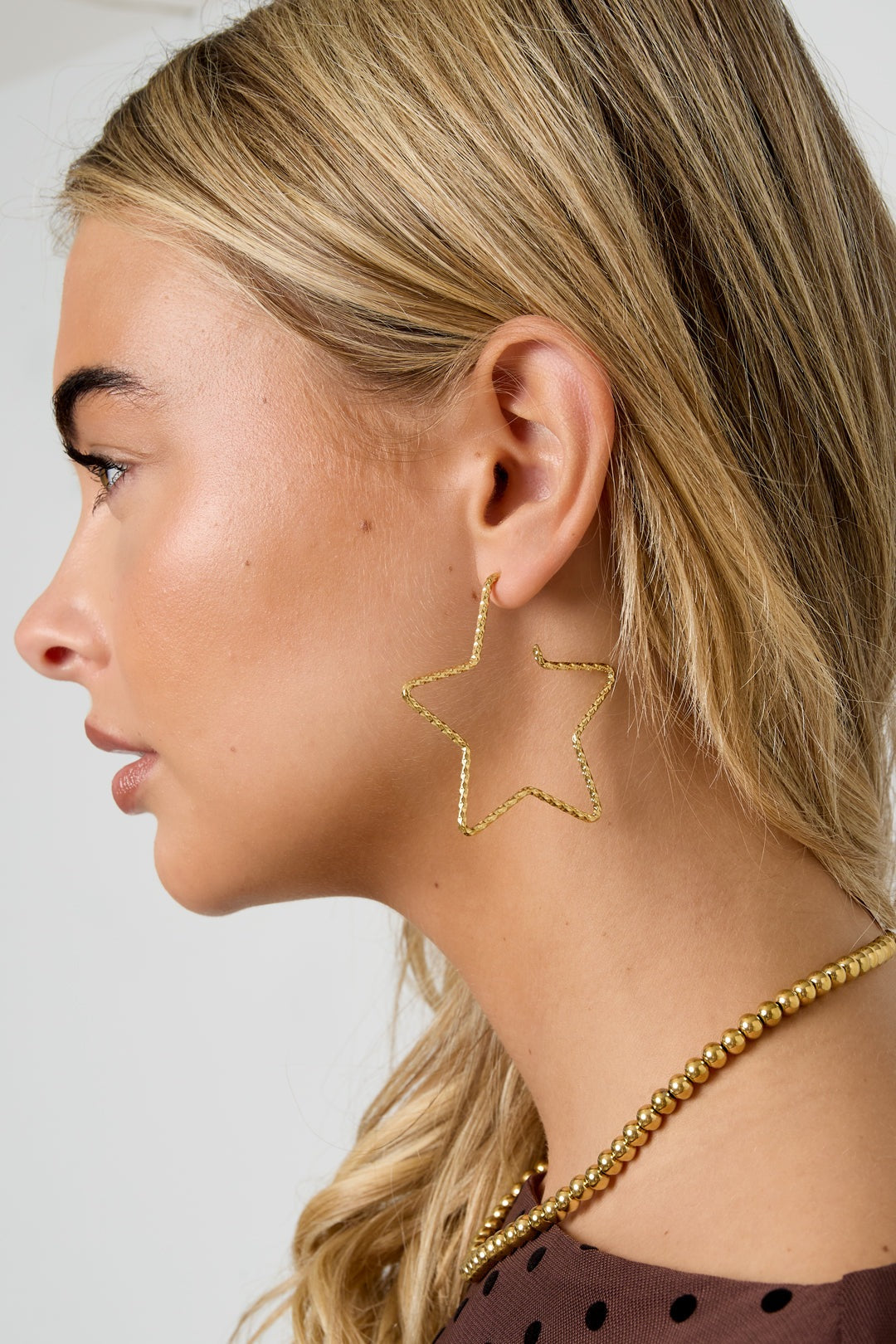 Another side angle of the gold star-shaped hoops on a model with long blonde hair