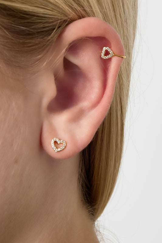 Close-up of ear featuring matching gold-tone heart-shaped stud and upper ear cuff with zircon crystals