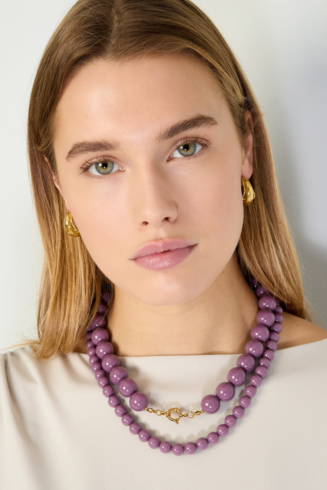 Model wearing double-layer purple chunky resin beaded necklace with gold clasp and matching gold earrings