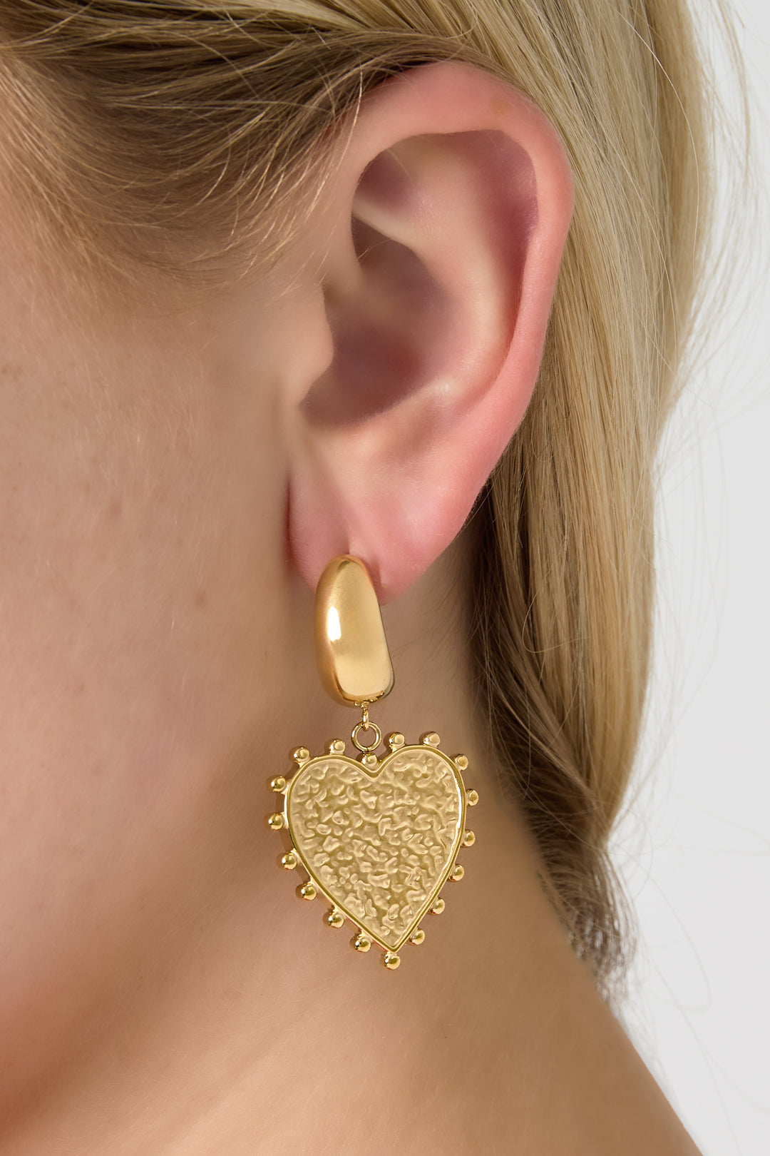 Close-up portrait showing gold modern heart drop earring worn by a woman