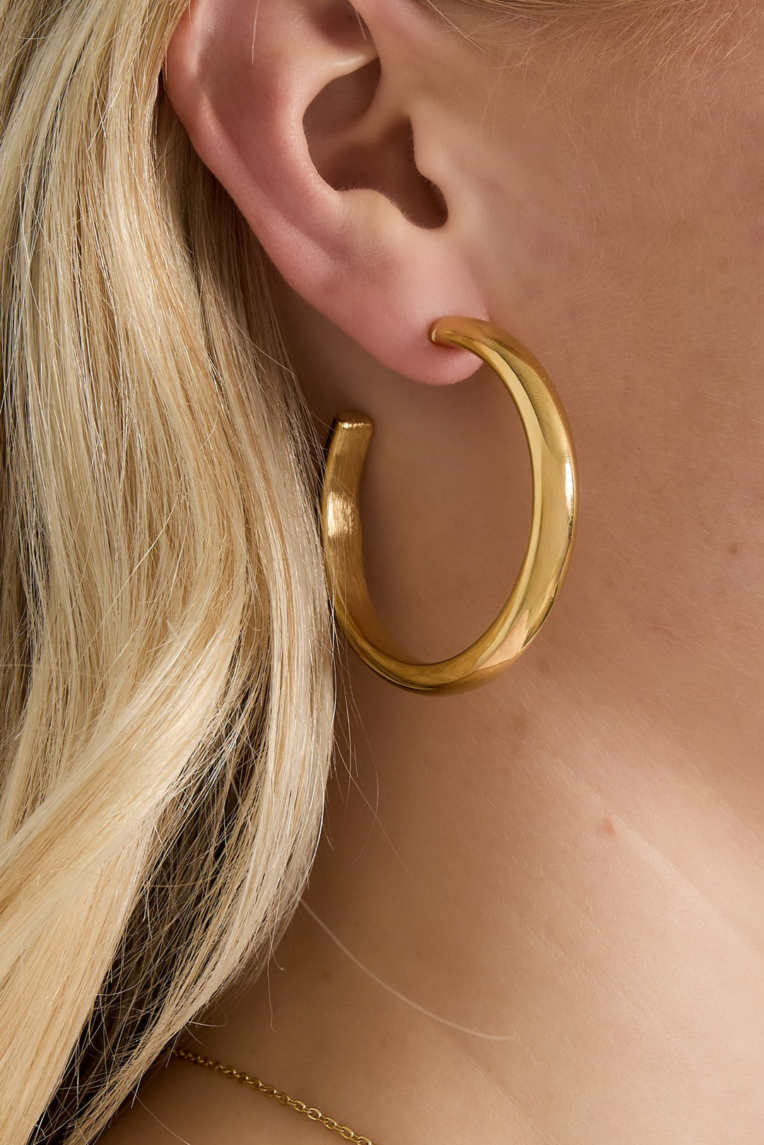 Close-up of gold chunky hoop earring worn by woman with blonde hair