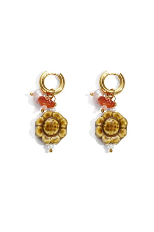 Pair of artisanal floral charm drop earrings with gold hoops, glazed honey-brown ceramic flower pendants, faux pearls, and coral beads laid flat on white background
