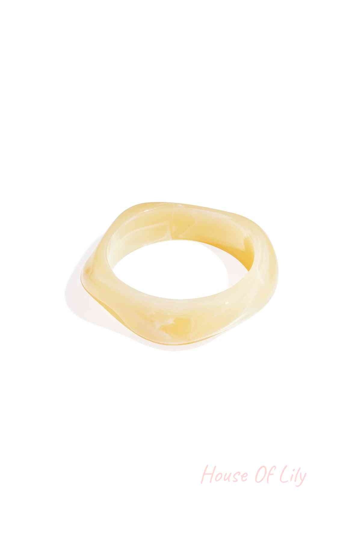 A pale yellow, wavy-edged acrylic statement bangle with a smooth, translucent marbled finish.