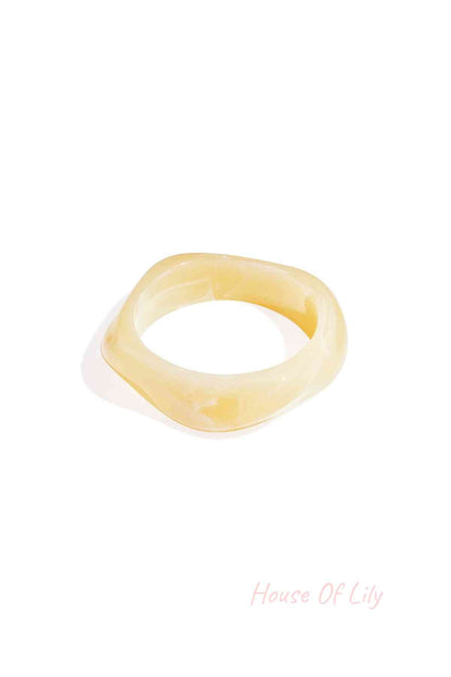 A pale yellow, wavy-edged acrylic statement bangle with a smooth, translucent marbled finish.