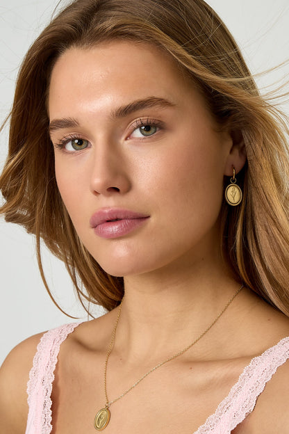 Woman wearing gold floral oval hoop earrings with matching pendant necklace