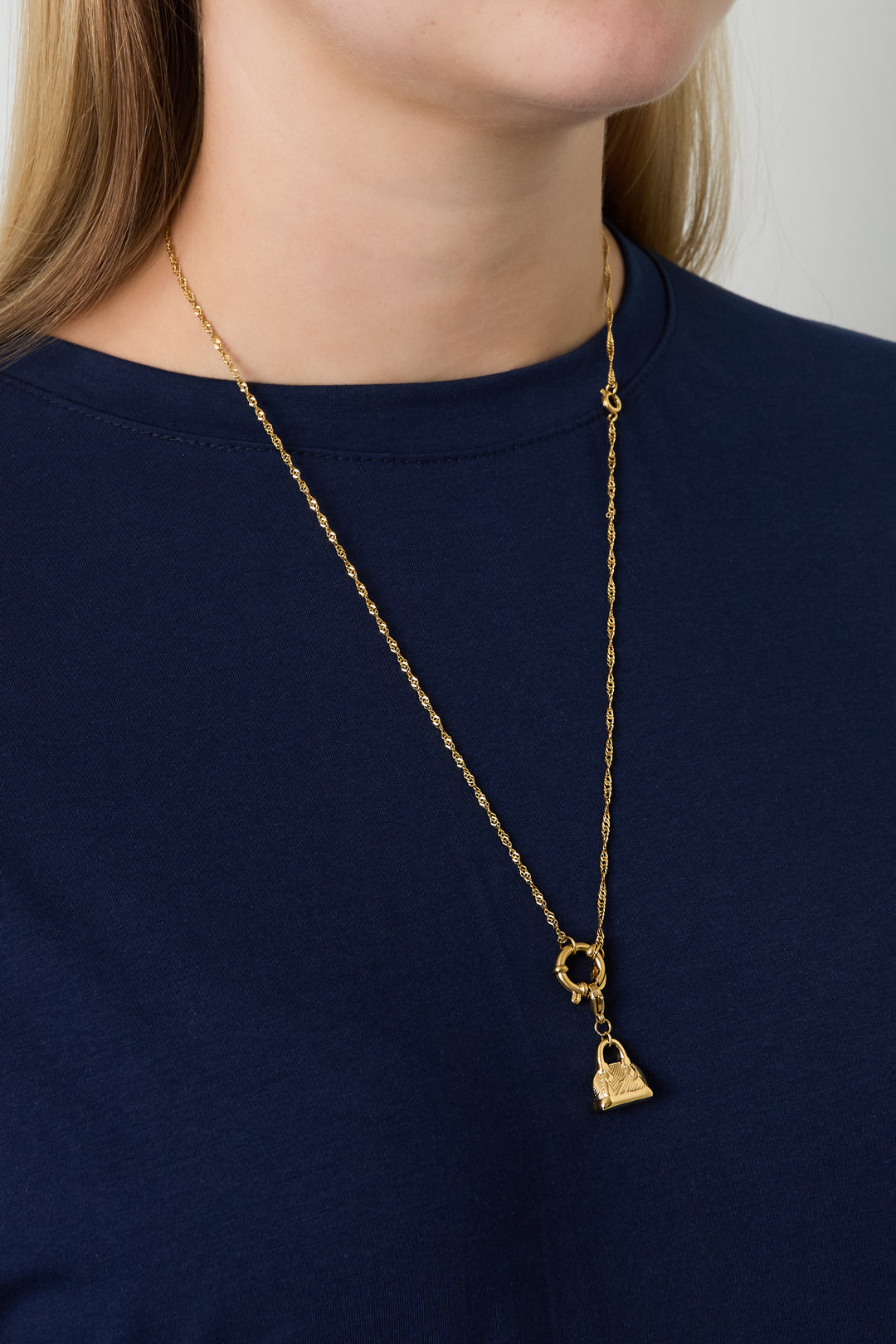 Model wearing gold chain necklace with a small handbag charm over navy top