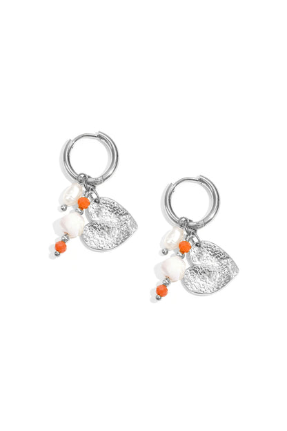 Pair of silver hoop earrings featuring hammered heart charm, pearls, and small orange and white beads on a white background