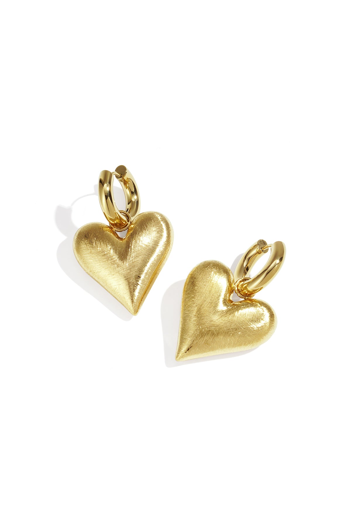 Pair of gold heart charm drop earrings with brushed texture on white background
