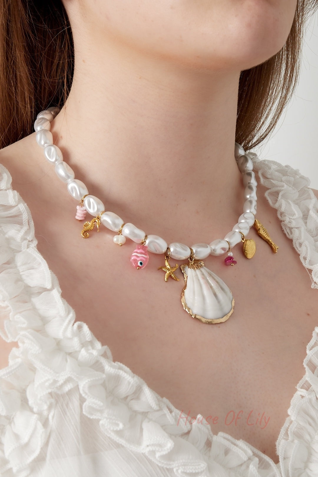 Close-up of a woman wearing the white pearl necklace with nautical gold and pink charms paired with a white ruffled blouse