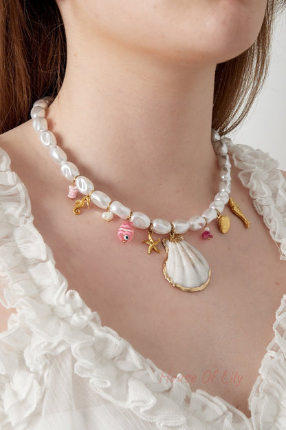 Close-up of a woman wearing the white pearl necklace with nautical gold and pink charms paired with a white ruffled blouse