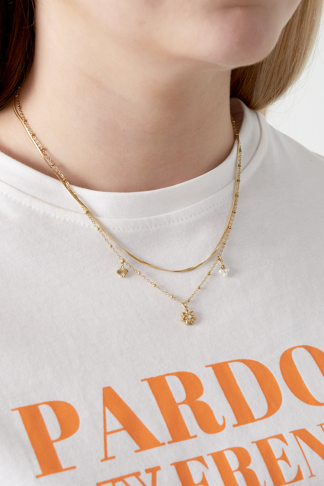 Close-up of a woman wearing a gold layered flower charm necklace with a white t-shirt