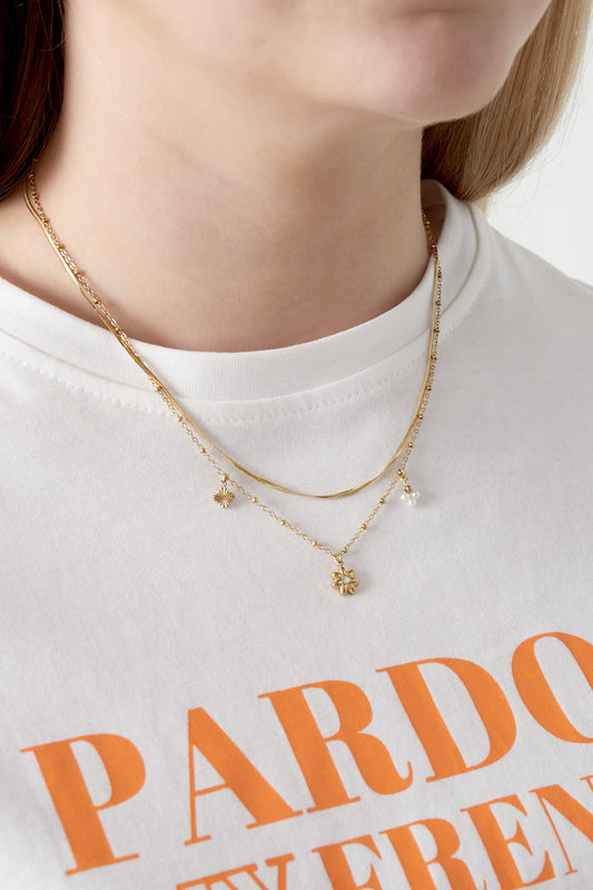Close-up of a woman wearing a gold layered flower charm necklace with a white t-shirt