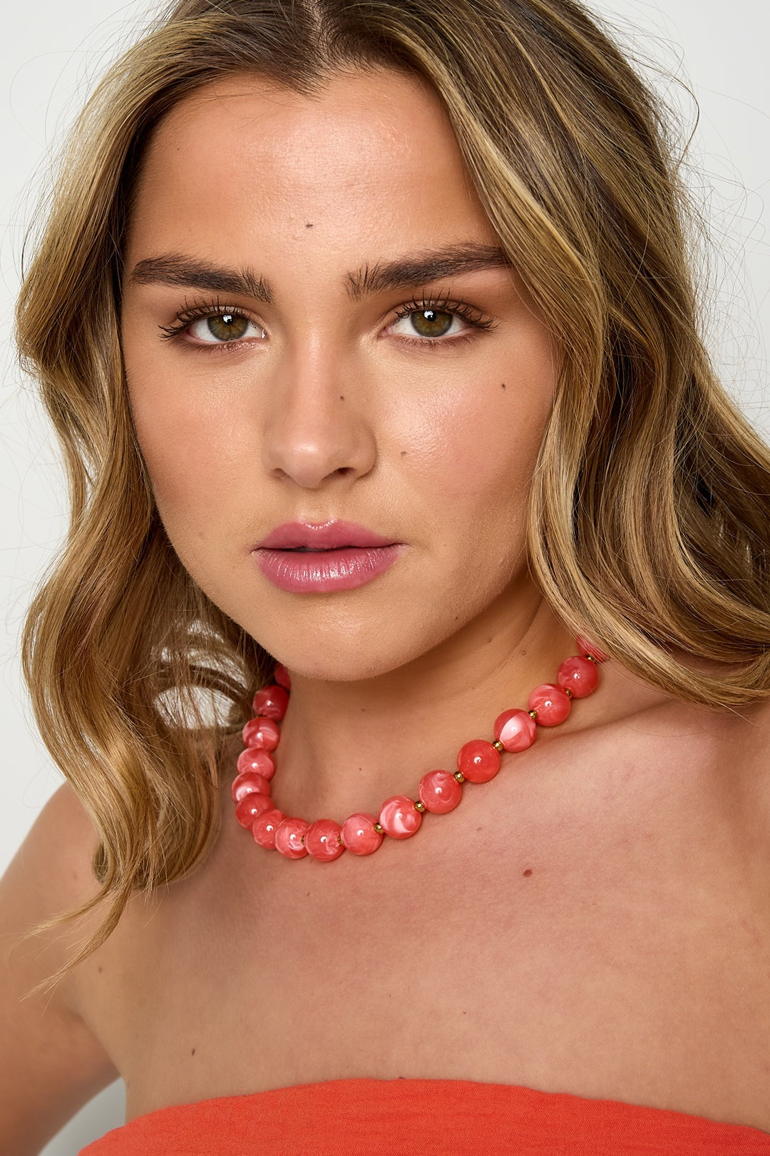 Close-up portrait of woman with coral pink chunky beaded necklace wearing coral tube top