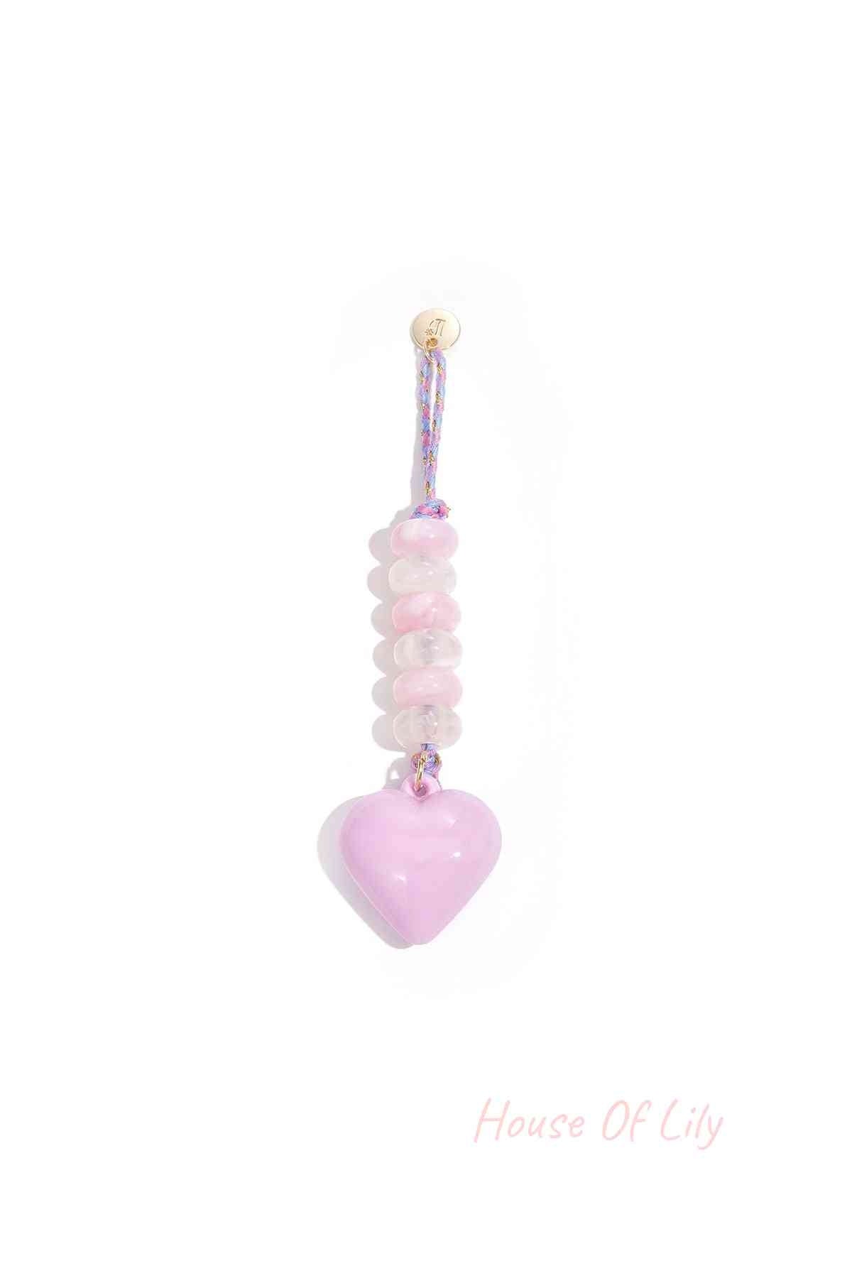 Lavender heart-shaped acrylic bag charm with translucent purple and lavender beads on braided purple and gold loop hanging against white background.