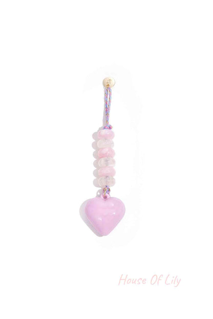 Lavender heart-shaped acrylic bag charm with translucent purple and lavender beads on braided purple and gold loop hanging against white background.