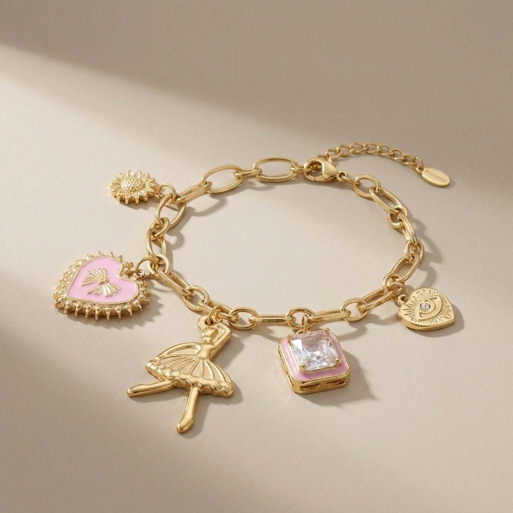 Gold charm bracelet with pink enamel heart, ballerina, crystal, sun, and evil eye charms on a chunky chain.