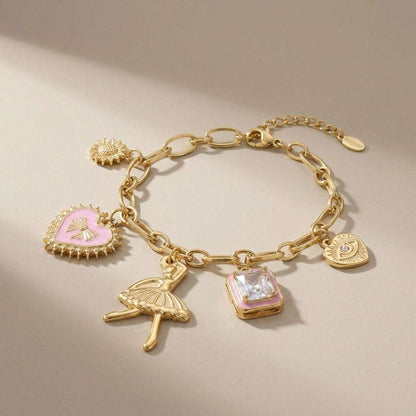 Gold charm bracelet with pink enamel heart, ballerina, crystal, sun, and evil eye charms on a chunky chain.