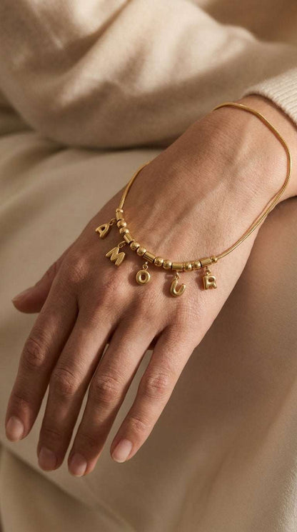 Gold chain bracelet with dangling letter charms spelling "AMOUR" on a person's wrist.