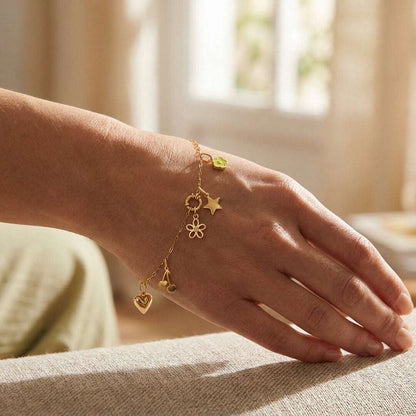 Gold charm bracelet on a wrist featuring a heart, cherry, flower, star, and small lime green enamel flower charm.