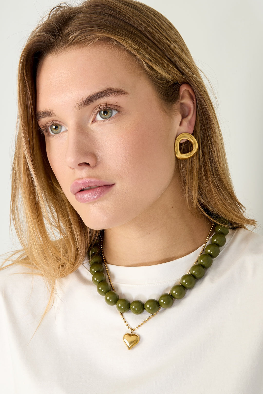 Model wearing olive green chunky bead necklace layered with heart pendant necklace and gold irregular hoop earrings