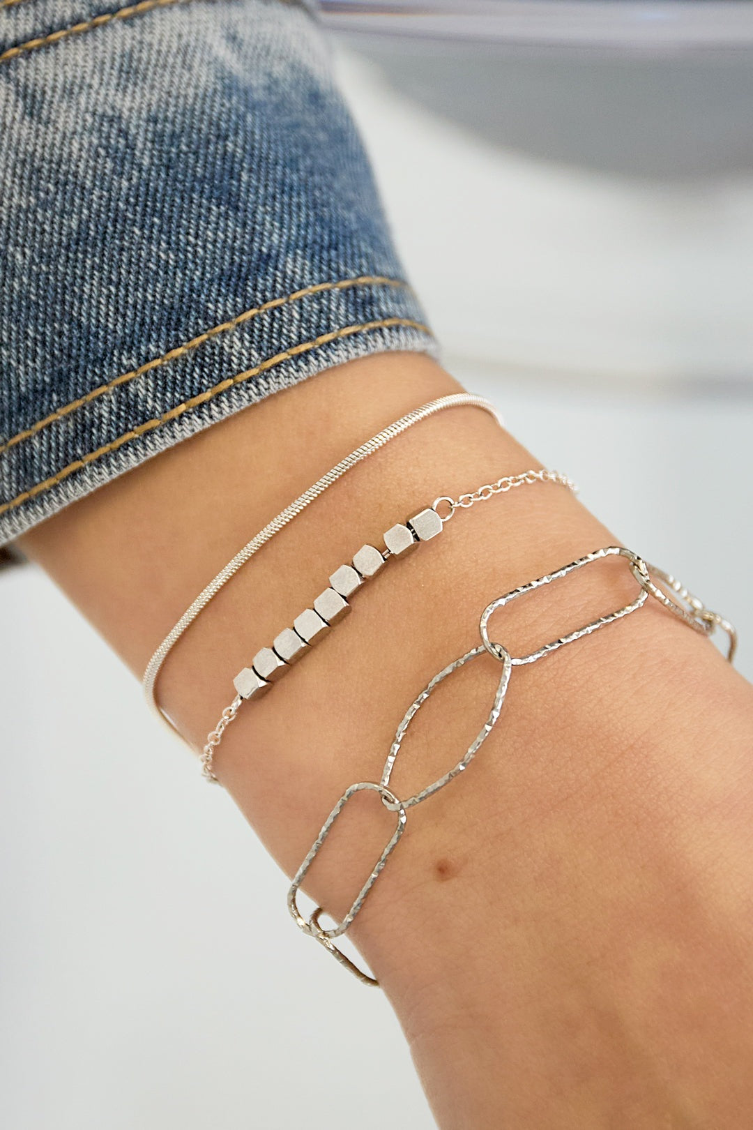 Close-up of wrist wearing layered bracelets including a silver textured chain link bracelet and others
