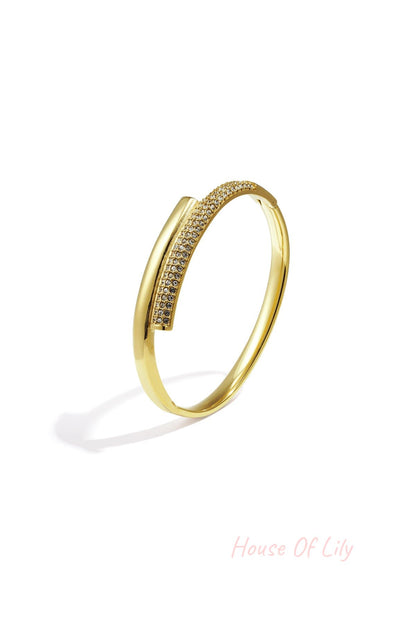 Close-up of gold-tone minimalist bangle with embedded crystals resting on white background