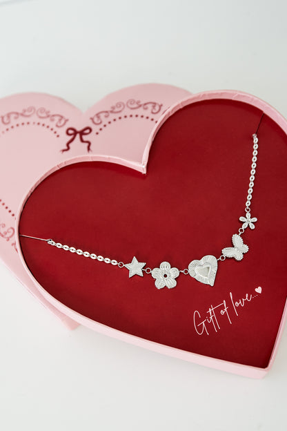 Close-up of silver charm pendant necklace showcasing detailed star, flower, heart, butterfly, and tiny flower charms on an adjustable chain inside the red heart-shaped box with pink trim