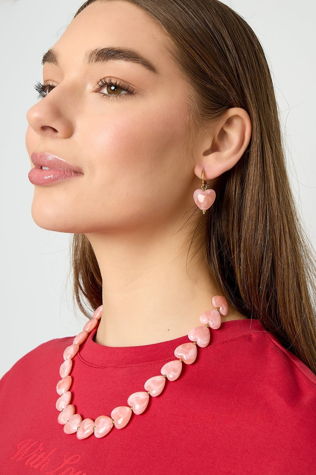 Model wearing peach resin heart earrings and matching heart necklace, paired with red top