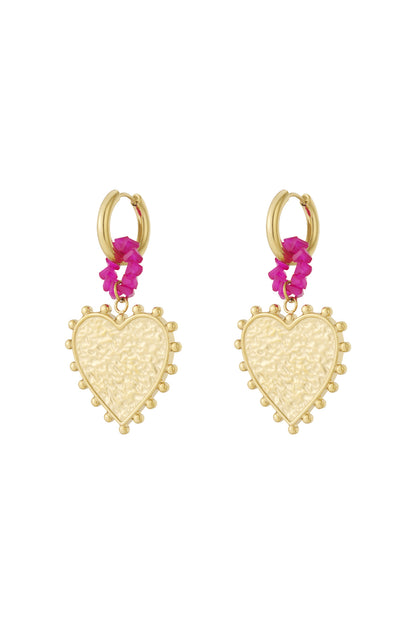 Pair of gold hoop earrings featuring textured heart-shaped pendants surrounded by ornamental dots and connected with bright pink beaded rings against white background